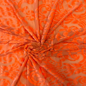 May include: Orange sheer fabric with a raised damask pattern. The fabric is soft and flowing, making it ideal for draping or creating garments.