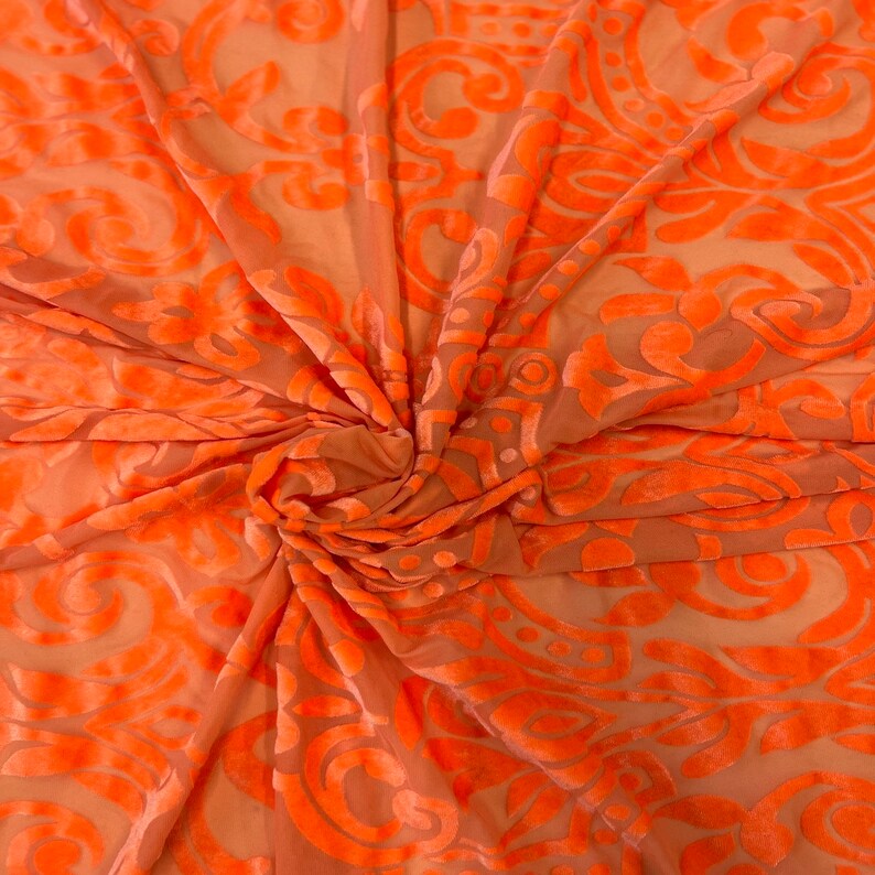 May include: Orange sheer fabric with a raised damask pattern. The fabric is soft and flowing, making it ideal for draping or creating garments.