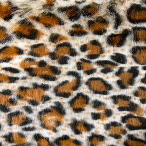 May include: Close-up of a brown, black, and white faux fur fabric with a leopard print pattern.