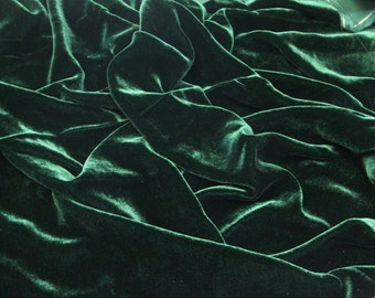 May include: A close-up of a deep green velvet fabric with a soft, luxurious texture. The fabric is draped and folded, creating a rich and elegant look.