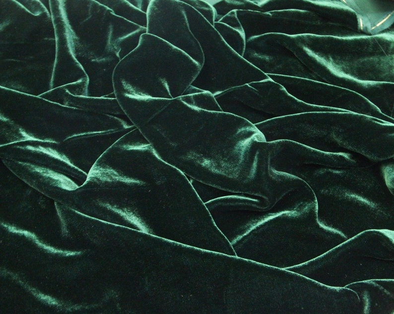 May include: A close-up of a deep green velvet fabric with a soft, luxurious texture. The fabric is draped and folded, creating a rich and elegant look.