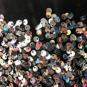 May include: A black fabric background covered in silver, red, and iridescent sequins.