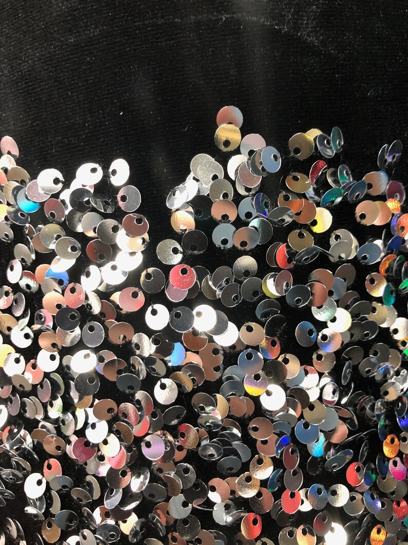 May include: A black fabric background covered in silver, red, and iridescent sequins.