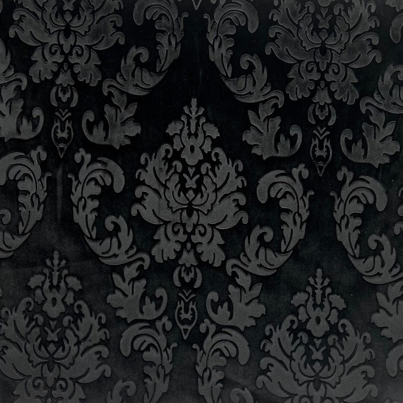 Pode incluir: Close-up de um tecido de veludo preto com um padr&atilde;o de damasco em relevo. O design apresenta folhas e motivos florais em espiral em um efeito tom sobre tom, criando uma textura luxuosa. A cor escura e o design intrincado sugerem um estilo cl&aacute;ssico e elegante.