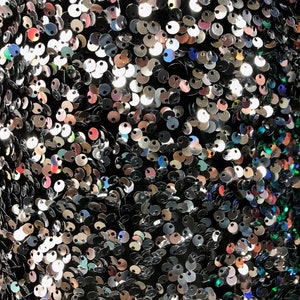 May include: A close-up of a fabric covered in iridescent sequins. The sequins are silver, black, and blue.