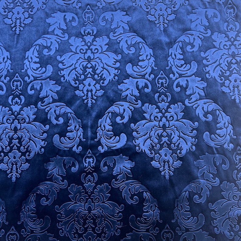 K&ouml;nnte beinhalten: Nahaufnahme eines dunkelblauen Stoffes mit einem gepr&auml;gten Damastmuster. Der Stoff hat eine weiche, samtige Textur.