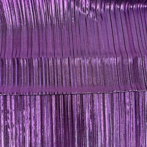 May include: Close-up of a shiny, pleated fabric in a vibrant shade of purple. The material has vertical lines and a metallic sheen, creating a textured and reflective surface. The fabric appears to be gathered or folded, adding depth and dimension.