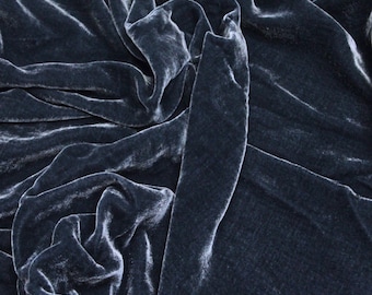 May include: A close-up of a soft, blue velvet fabric with a smooth, silky texture. The fabric is draped and folded, creating a luxurious and elegant look.