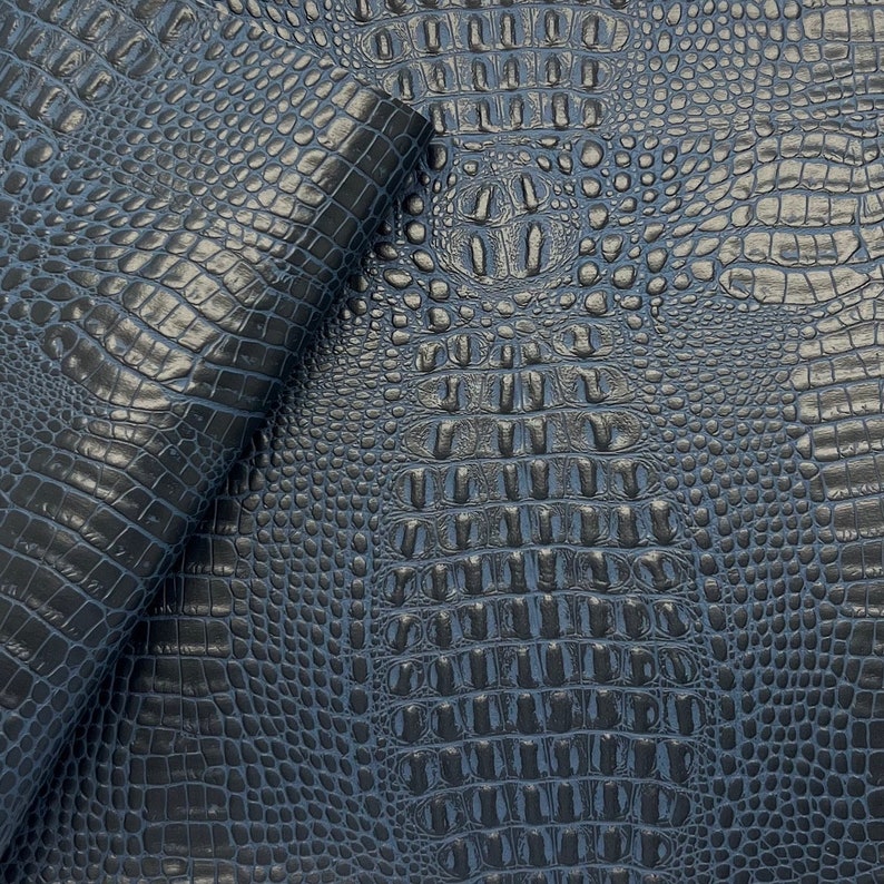 Puede incluir: Primer plano de una tela de imitaci&oacute;n de piel de cocodrilo azul oscuro. La tela tiene un patr&oacute;n texturizado y en relieve que se asemeja a escamas de cocodrilo.
