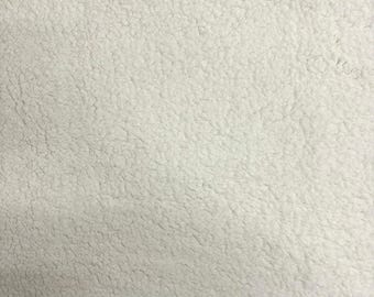 May include: A close-up view of a white, textured fabric with a dense, curly, and soft pile surface. The material features a consistent, uniform off-white color throughout, creating a plush, fleece-like appearance with a thick, fuzzy, and looped texture.