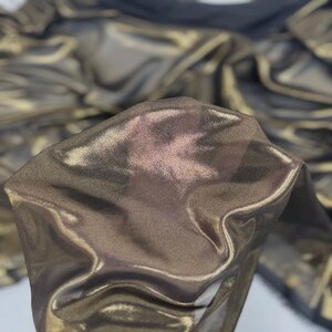 May include: Close-up of shimmering fabric with a metallic sheen. The material is a blend of gold and bronze tones, creating a luxurious and fluid appearance. The fabric appears soft and drapes gracefully, suggesting it could be used for apparel or decorative purposes.