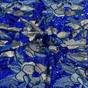 May include: Blue and silver sequined fabric with a floral pattern. The sequins are arranged in a swirling design, creating a shimmering effect.