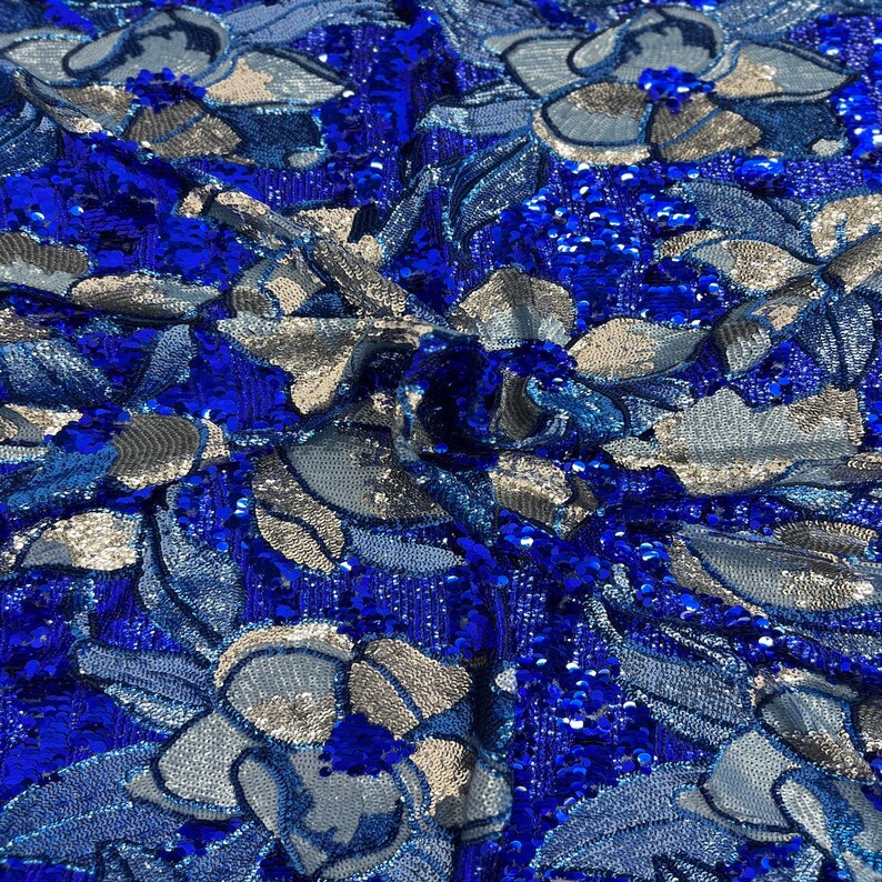 May include: Blue and silver sequined fabric with a floral pattern. The sequins are arranged in a swirling design, creating a shimmering effect.