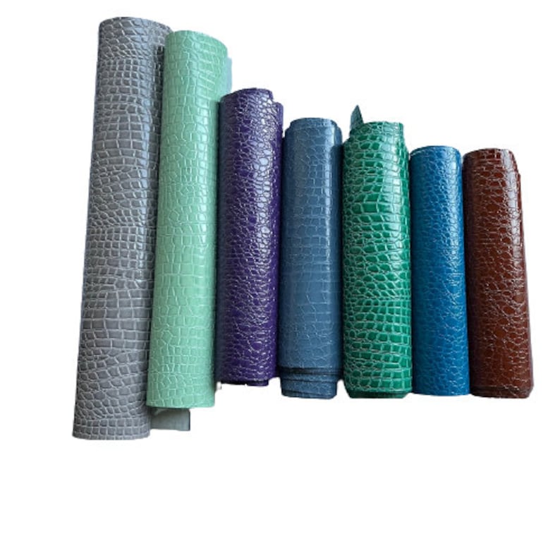 May include: A collection of eight rolls of faux leather in various colors, including gray, green, purple, blue, and brown. The leather has a crocodile embossed pattern.