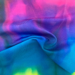 May include: A close-up of a blue, purple, and pink tie-dye fabric. The fabric is soft and has a smooth texture.