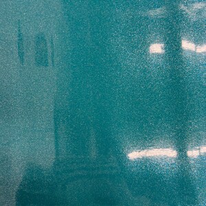 May include: A close-up of a teal blue surface with a sparkly, textured finish. The surface reflects light, creating a shimmering effect.