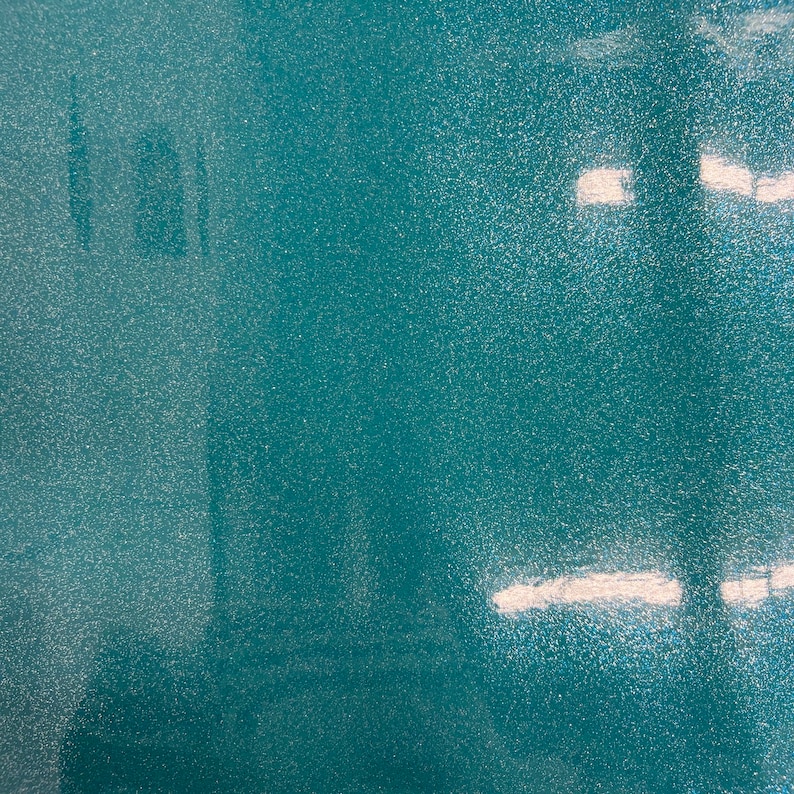 May include: A close-up of a teal blue surface with a sparkly, textured finish. The surface reflects light, creating a shimmering effect.