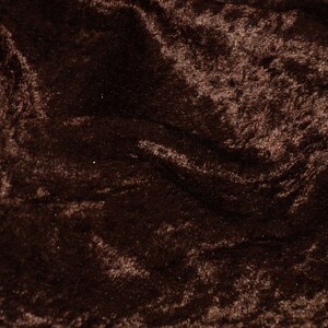 May include: Close-up of a brown velvet fabric with a soft, plush texture. The fabric is wrinkled and has a subtle sheen.