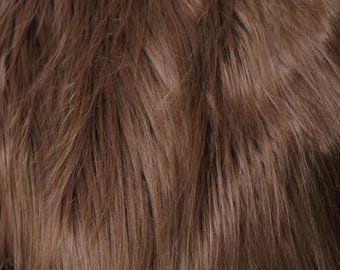 May include: A dense, long-pile faux fur fabric in a solid medium brown color. The texture consists of numerous fine, straight, and slightly wavy fibers that create a layered, shaggy appearance with subtle variations in light and shadow.
