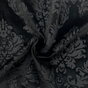 Pode incluir: Close-up de tecido preto com um padr&atilde;o de damasco em relevo. O tecido est&aacute; dobrado, criando sombras e destacando a textura do design. O padr&atilde;o apresenta folhas e motivos florais.