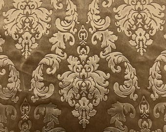 May include: A fabric featuring a repeating damask pattern in shades of brown and tan. The design consists of symmetrical, ornate floral and leaf motifs with a raised texture, set against a smooth, darker brown background surface.