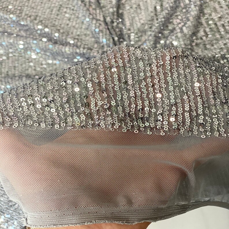 May include: Silver sequined fabric with a sheer mesh backing. The sequins are arranged in vertical rows.