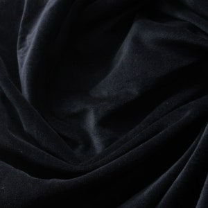 May include: Close-up of a black velvet fabric with soft folds and wrinkles. The fabric has a smooth, luxurious texture.