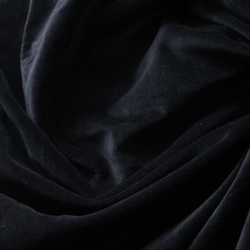 May include: Close-up of a black velvet fabric with soft folds and wrinkles. The fabric has a smooth, luxurious texture.