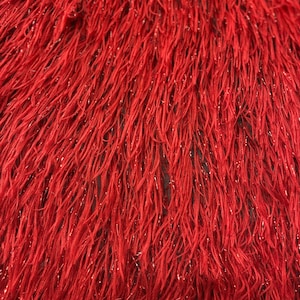 May include: Red sparkly fabric with a fuzzy texture. The fabric is made of thin strands of yarn that are woven together to create a soft, plush surface.
