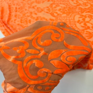 May include: Orange and brown fabric with a damask pattern. The fabric is sheer and has a velvety texture.