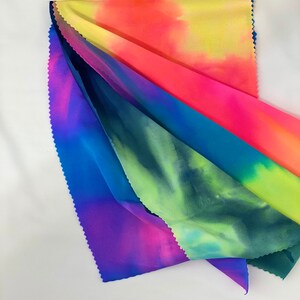 May include: Four different tie-dye fabrics in shades of blue, green, pink, and yellow. The fabrics are folded and layered on top of each other.
