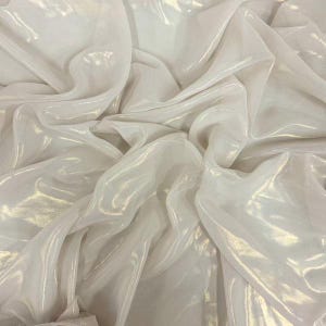 May include: Close-up of a white, shimmering fabric with soft folds and highlights. The material appears lightweight and translucent, with a subtle sheen that catches the light, creating a flowing, elegant appearance.
