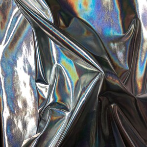 May include: Close-up of iridescent silver fabric with a textured surface. The fabric is folded and draped, creating a dynamic and abstract pattern.
