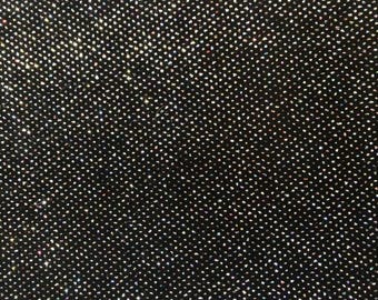 May include: A black fabric surface featuring a dense, uniform pattern of small, reflective, multi-colored glitter particles that catch the light, creating a shimmering, textured appearance across the entire visible area of the material.