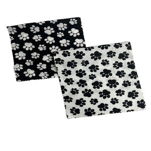 May include: Two black and white fabric squares with a paw print pattern. The top square has white paw prints on a black background. The bottom square has black paw prints on a white background.