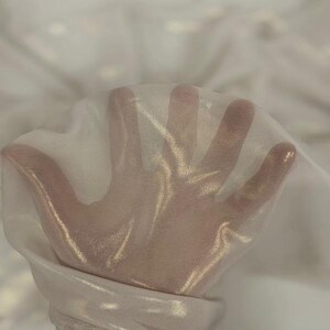 May include: A close-up of a sheer, white fabric held up, allowing light to pass through. The fabric is slightly wrinkled, creating soft shadows and highlights. The material appears delicate and lightweight, suitable for apparel or decorative purposes.