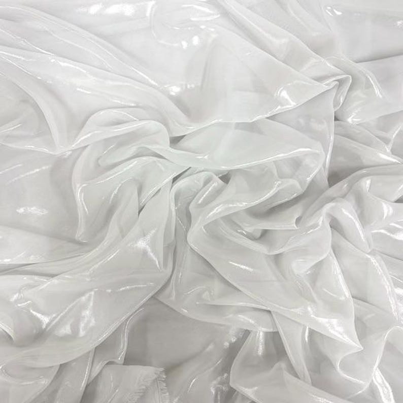 May include: A close-up of white, shimmering fabric, with folds and creases creating a textured effect. The material appears to be lightweight and possibly translucent, with a subtle sheen. The fabric is likely suitable for clothing or decorative applications.