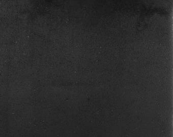 May include: A solid, square-shaped tile with a matte black finish. The surface features a fine, uniform, slightly granular texture that absorbs light, creating a consistent dark appearance across the entire flat, non-reflective plane.
