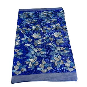 May include: Blue fabric with a silver floral pattern. The fabric is covered in sequins and has a shimmery finish.