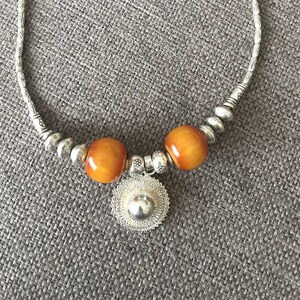 May include: A silver necklace with two amber beads and a silver pendant. The pendant is a round, openwork design.