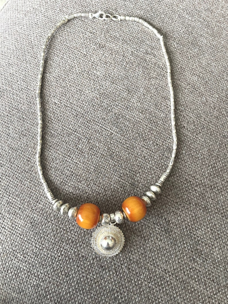 May include: A silver necklace with two amber beads and a silver pendant. The pendant is a round, openwork design.