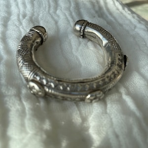 May include: A silver bangle bracelet with intricate etched designs and a rounded edge. The bracelet is made of metal and has a polished finish.