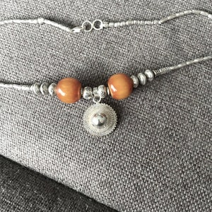 May include: A silver chain necklace with two brown wooden beads and a silver pendant with a circular design.