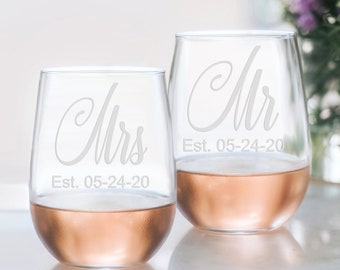 May include: Two clear glass wine glasses with the words "Mr. Est. 05-24-20" and "Mrs. Est. 05-24-20" etched on them. The glasses are filled with a light pink beverage.