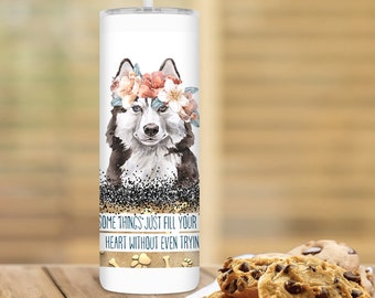 May include: White stainless steel tumbler with a black and white husky dog wearing a floral crown. The tumbler has the text "Some things just fill your heart without even tryin'" and paw prints and bone graphics.