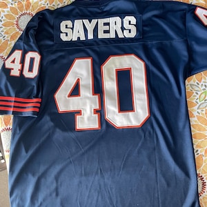May include: A navy blue football jersey with the name "SAYERS" across the shoulders and the number "40" on the front, back, and sleeves. The numbers are white with orange trim. The sleeves have orange and white stripes.