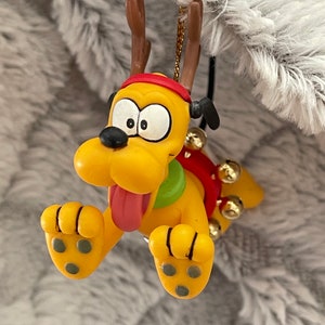 May include: Yellow cartoon dog Christmas ornament with red antlers, a red and green scarf, and gold jingle bells.