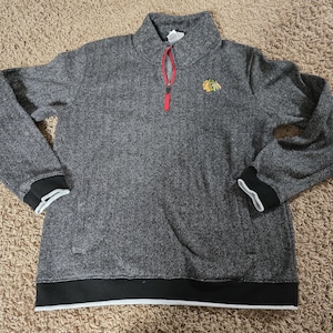 May include: A gray herringbone-patterned pullover sweatshirt with a red zipper and a small logo on the chest. The cuffs and hem are black with white trim. The collar is a mock neck style.
