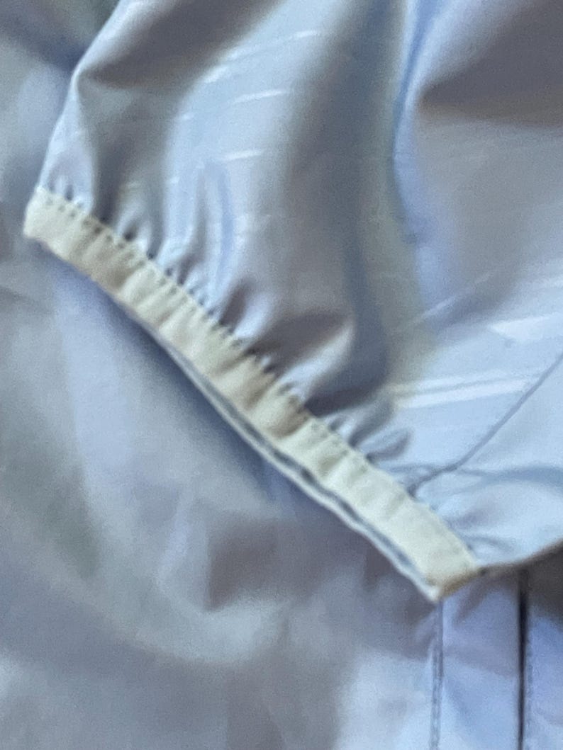 K&ouml;nnte beinhalten: Nahaufnahme des hellblauen &Auml;rmels einer Jacke mit wei&szlig;em Besatz. Der Stoff hat ein dezentes Muster.