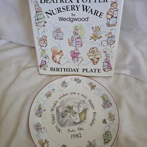 May include: A Beatrix Potter Nursery Ware birthday plate and box. The plate features a central illustration with the text "Mrs. Tiggy-Winkle wishes you a very Happy Birthday" and "1982". The box has illustrations of Beatrix Potter characters.